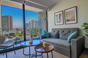 A modern living room with a grey sofa, two armchairs, a round coffee table, and a view of a cityscape through large windows. - Apartamento 2BR/1BA con Vista Cordillera y Ciudad, Wifi (Santiago)