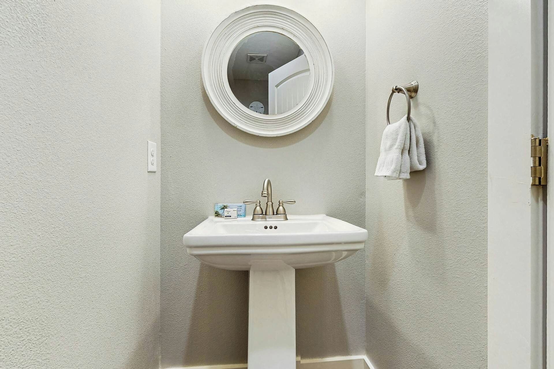 Un baño con un lavamanos blanco de pedestal, un espejo redondo y un perchero para toallas.