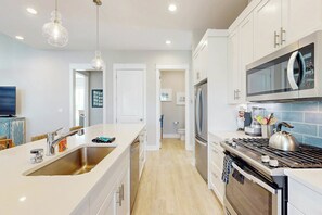 A modern kitchen with a central island, stainless steel appliances, and a microwave above the stove. - Crab Manor | Steps to Beach | Resort Amenities (Port Aransas)