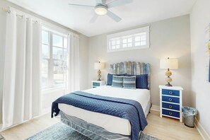 Quarto com cama, duas mesas de cabeceira, ventoinha no teto e janela.