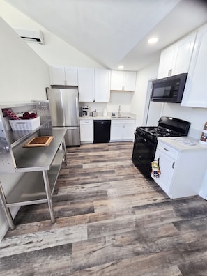 A modern kitchen with stainless steel appliances, white cabinetry, and a herringbone wood floor. - Walk to Ocean Beach & Sunset Cliffs, King Bed & AC (San Diego)