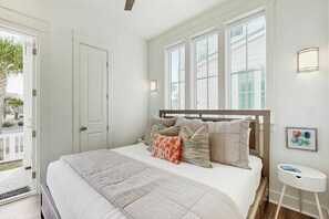 A bedroom with a bed, a bedside table, a window, and a door. - Beach Happy | Steps to Beach | Resort Amenities (Port Aransas)