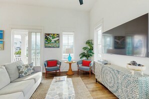 Ein Wohnzimmer mit einer Couch, zwei Sesseln, einem Couchtisch, einem gemusterten Teppich, einem Blumentopf und Kunstwerken an den Wänden.