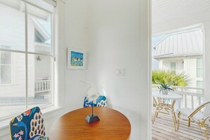 Ein Zimmer mit einem runden Holztisch, einem weißen Stuhl und einem Stuhl mit Pfauenmotiv. An der Wand hängt ein gerahmtes Bild und auf dem Tisch steht eine weiße Skulptur.
