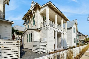 A two-story house with a balcony, a covered porch, and a fenced yard. - Beach Happy | Steps to Beach | Resort Amenities (Port Aransas)