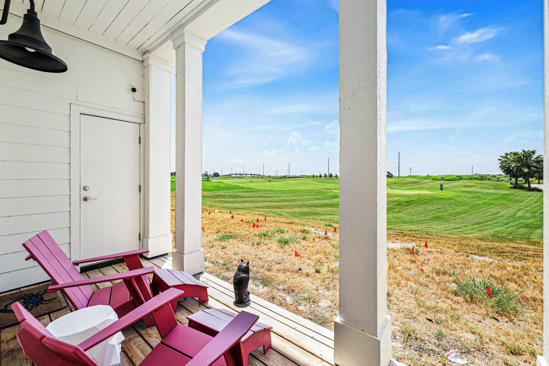 Eine Veranda mit roten Adirondack-Stühlen und einem Tisch, mit Blick auf einen Golfplatz.
