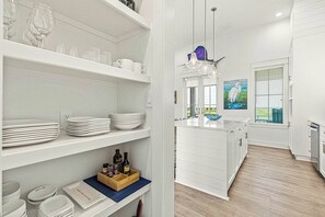 A modern kitchen with white cabinetry, a central island, and a view of the outdoors through a window. - Gone Coastal Casita 4 | Golf Views (Port Aransas)