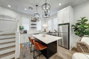 A modern kitchen with white cabinetry, a central island, stainless steel appliances, and pendant lighting. - Barefoot Bungalow | Golf Views | Steps to Beach (Port Aransas)