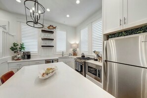 A modern kitchen with a central island, stainless steel appliances, and a pendant light fixture. - Barefoot Bungalow | Golf Views | Steps to Beach (Port Aransas)