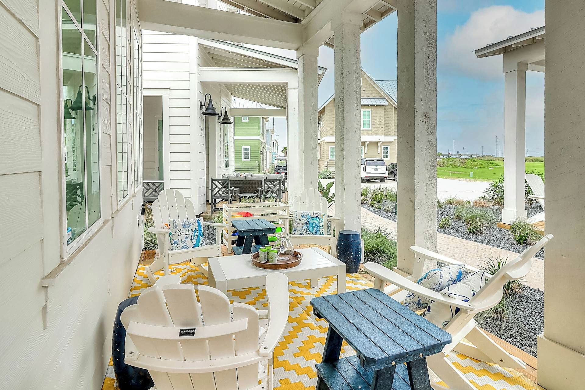 An outdoor patio area with white Adirondack chairs, a wooden table, and a yellow and white patterned floor.