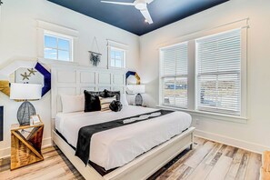 A bedroom with a bed, bedside tables, a ceiling fan, and a window with blinds. - Glam Wave | Gulf Views | Steps to Beach (Port Aransas)