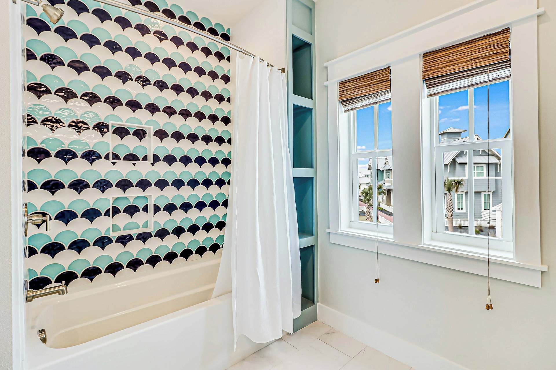 A bathroom with a bathtub, a shower with a patterned wall, and a window with a view of houses.