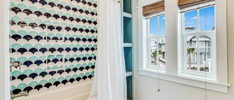 A bathroom with a bathtub, a shower with a patterned wall, and a window with a view of houses.