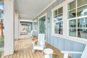 A covered porch with wooden flooring, white Adirondack chairs, and large windows. - Beachin' Bungalow | Gulf Views | Steps to Beach (Port Aransas)
