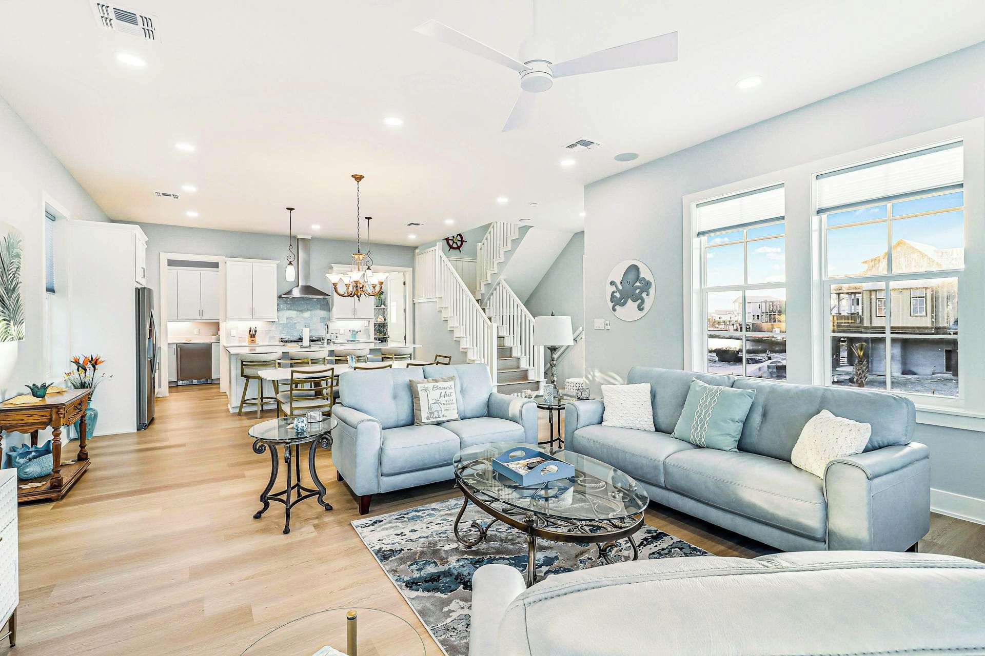 A spacious living area with a large window, a staircase, and a kitchen in the background.