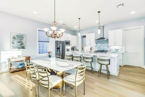 A modern kitchen with a central island, stainless steel appliances, and a dining area with a white table and gold chairs. - Allen's Anchor | Pet Friendly | Steps to Beach (Port Aransas)