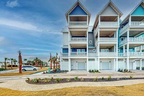 A multi-story hotel with balconies, a parking area, and palm trees. - Grand Rising | Gulf Views | Private Elevator (Port Aransas)
