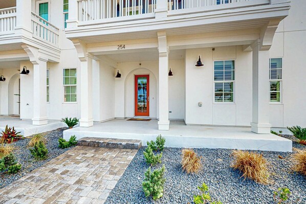 A two-story building with a red door, white columns, and a covered porch. - Grand Rising | Gulf Views | Private Elevator (Port Aransas)
