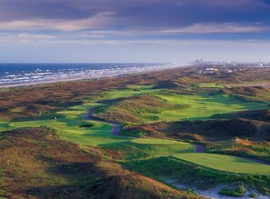 A coastal golf course with a view of the ocean and a distant city skyline. - Grand Rising | Gulf Views | Private Elevator (Port Aransas)