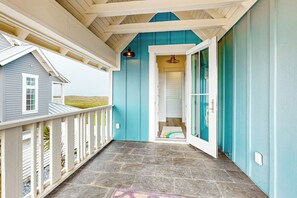 Een overdekte veranda met een stenen vloer, uitzicht op een huis en een deur die naar een kamer leidt.