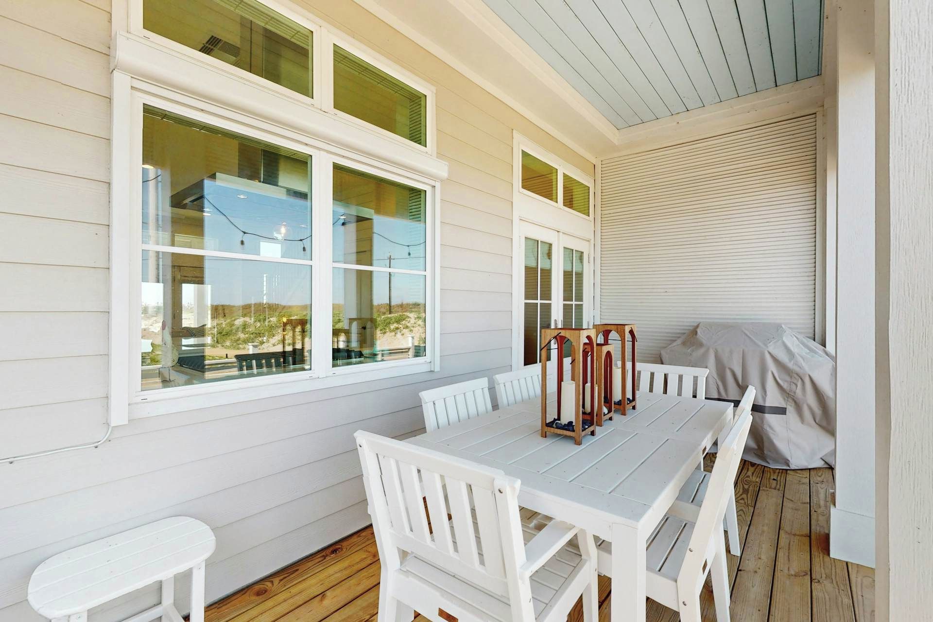 A covered patio with a white table and chairs, large windows, and a view of the landscape.