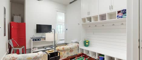 Een kamer met een tafelvoetbalspel, een televisie, een rode kast en een witte wandplank met haken.