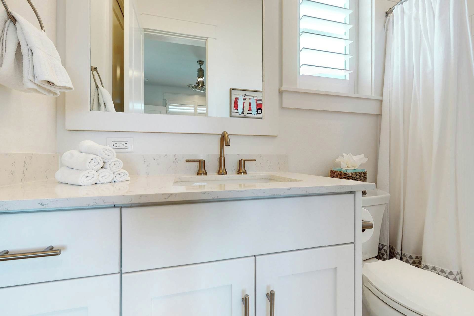 A bathroom with a white vanity, a sink with a gold faucet, a mirror, and a towel rack.