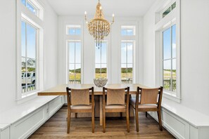 Spiseområde med et træbord og stole, en lysekrone og store vinduer med udsigt til det fri.