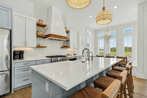 A modern kitchen with a large island, white cabinetry, and a view of the outdoors. - Casa Vela at Palmilla | Steps to Beach and Resort (Port Aransas)
