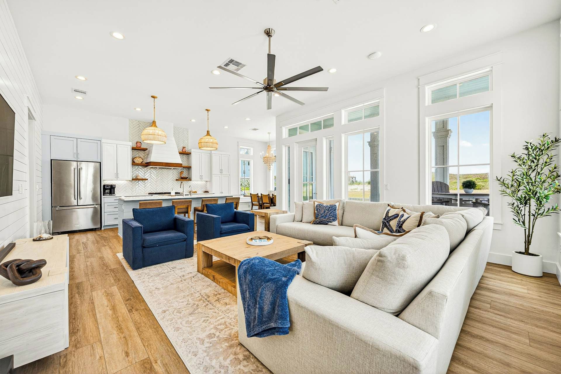 A spacious living area with a large sofa, blue armchairs, a wooden coffee table, and a ceiling fan.