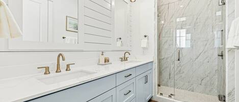 A modern bathroom with a large mirror, two sinks, and a shower area.