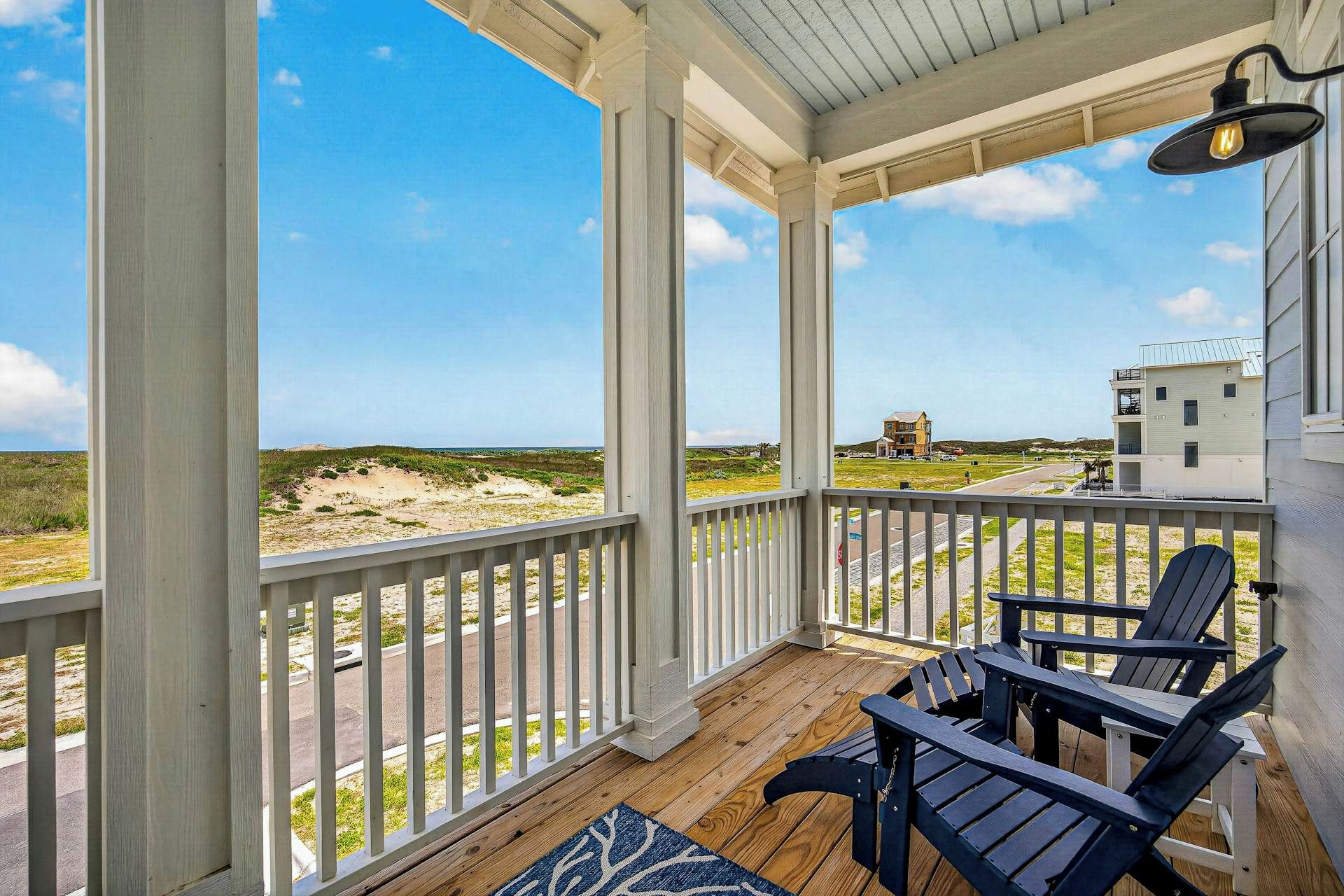 A covered porch with a view of the beach and a building in the distance.
