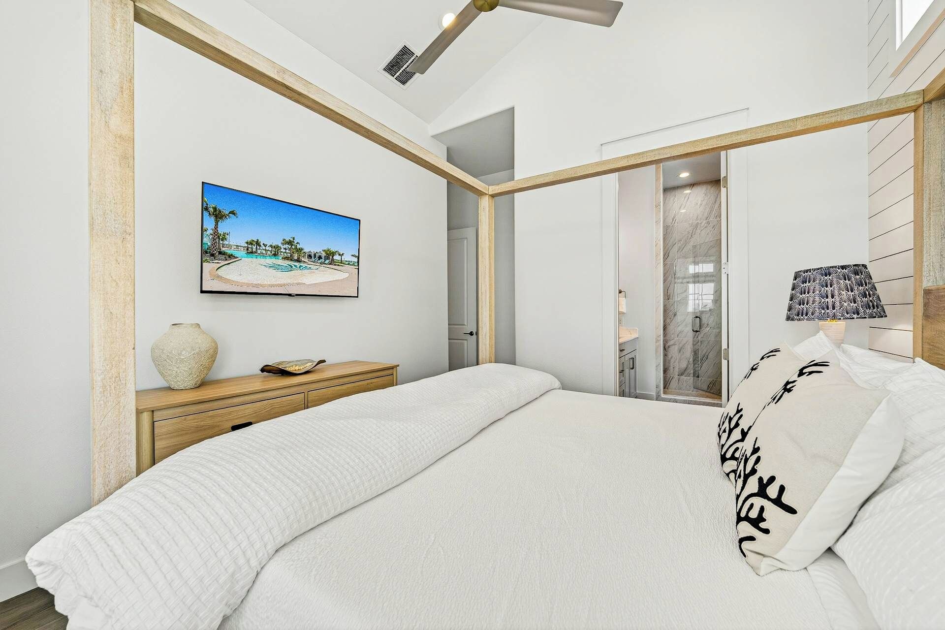 Une chambre à coucher comprenant un lit, une commode en bois, un téléviseur fixé au mur et une porte donnant sur une autre pièce.