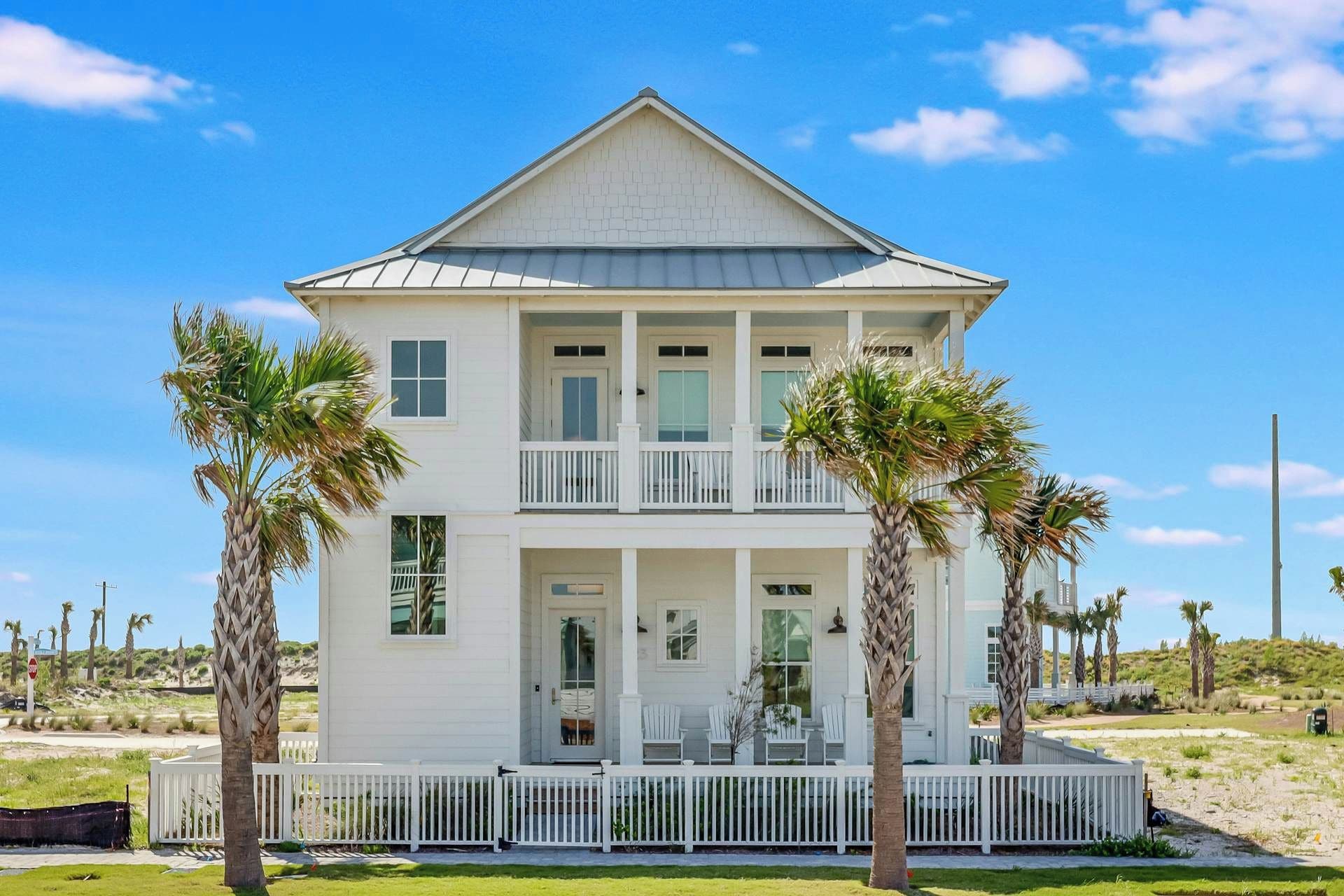 A two-story beachfront house with a balcony and a covered porch.