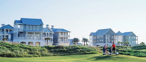 Een golfbaan met een clubhuis en grote huizen op de achtergrond.