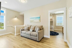 A living room with a beige sofa, a painting, and a staircase leading to another room. - Ocean Pearl | Pet Friendly | Steps to Beach (Port Aransas)