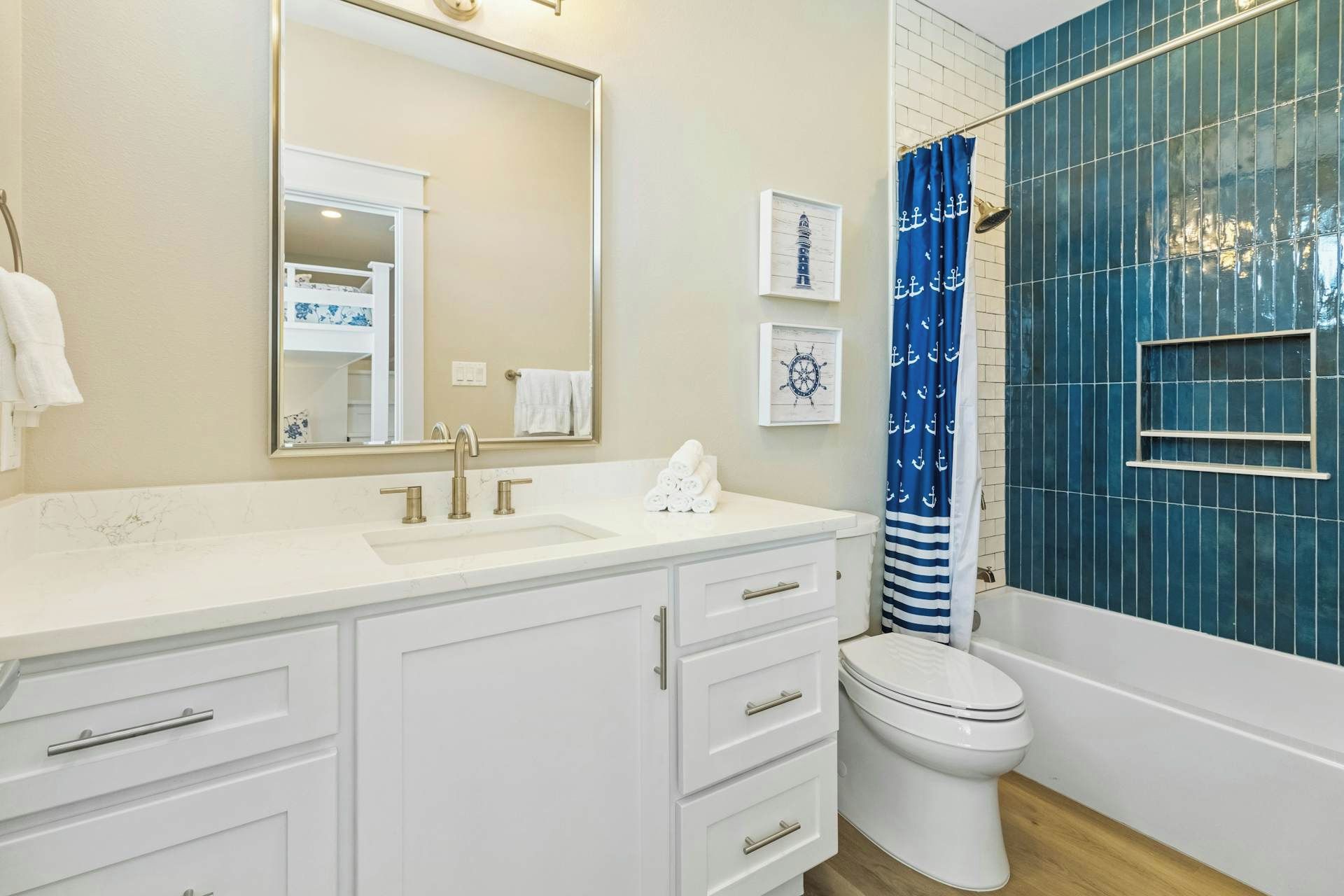 A bathroom with a white vanity, a large mirror, a toilet, and a shower with blue tiles.