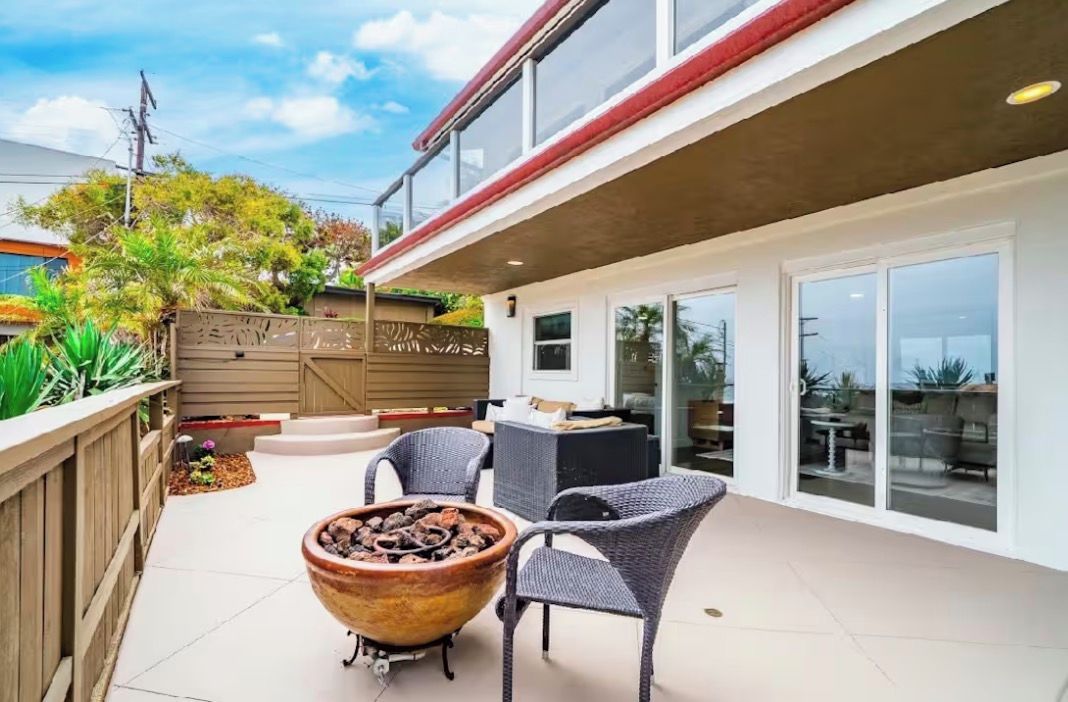 Un espace extérieur aménagé en terrasse, avec un foyer, des meubles en osier et une porte-fenêtre coulissante donnant sur un balcon.