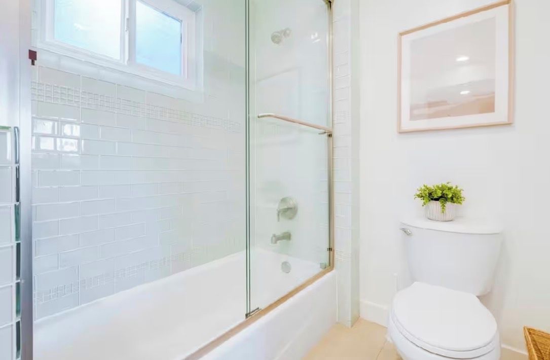 A bathroom with a glass-enclosed shower, a white toilet, and a framed picture on the wall.