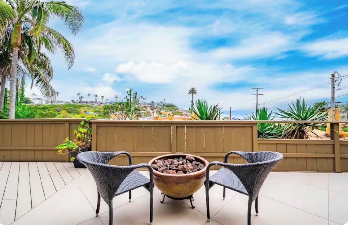 Eine Terrasse im Freien mit einem Feuerkorb, zwei Korbstühlen und Blick auf eine Küstenlandschaft.