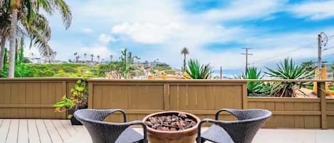 An outdoor patio with a fire pit, two wicker chairs, and a view of a coastal landscape.