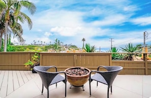 Eine Terrasse im Freien mit einem Feuerkorb, zwei Korbstühlen und Blick auf eine Küstenlandschaft.