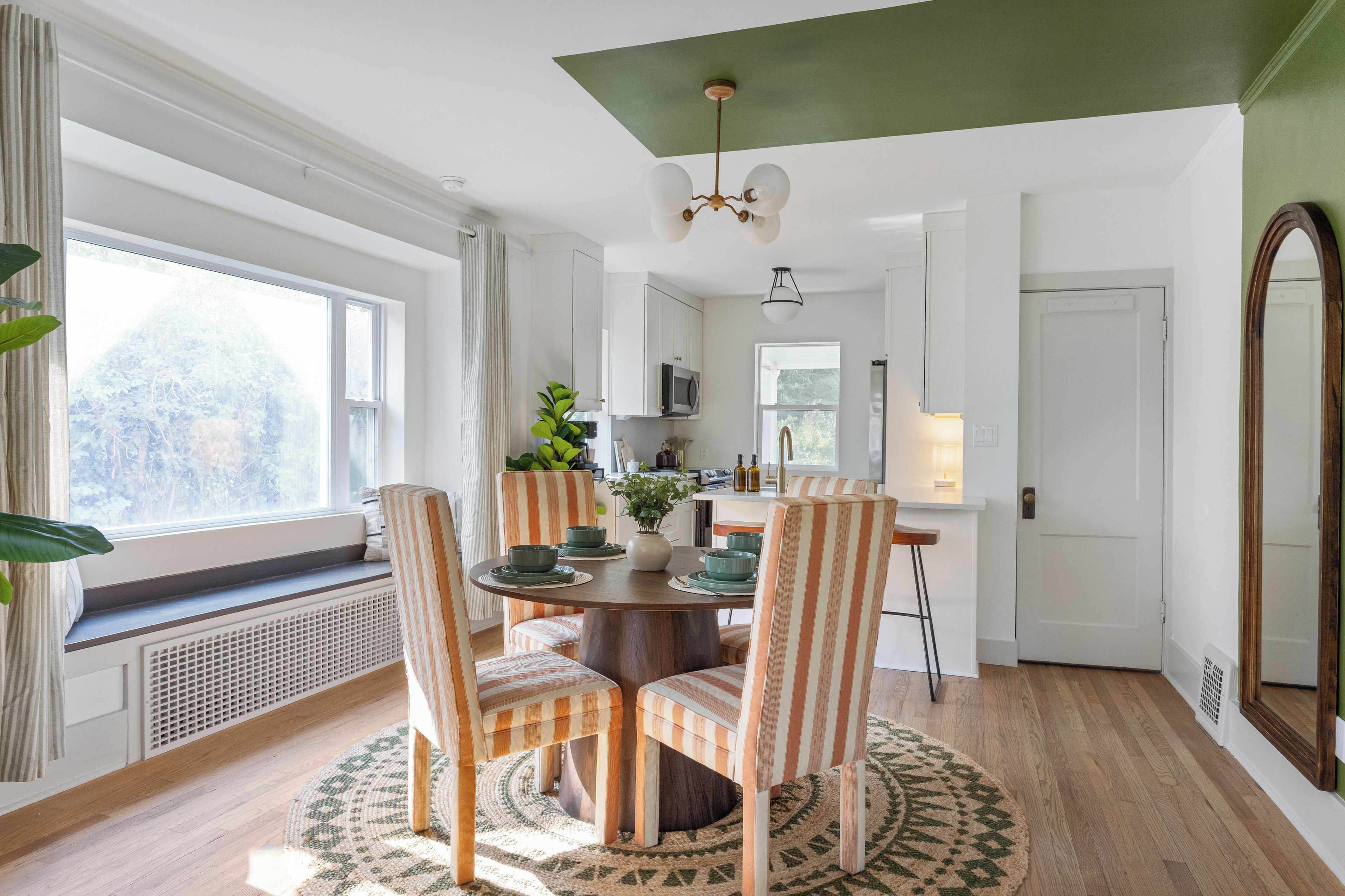 A dining area with a round table, striped chairs, and a view of the outdoors through a window.