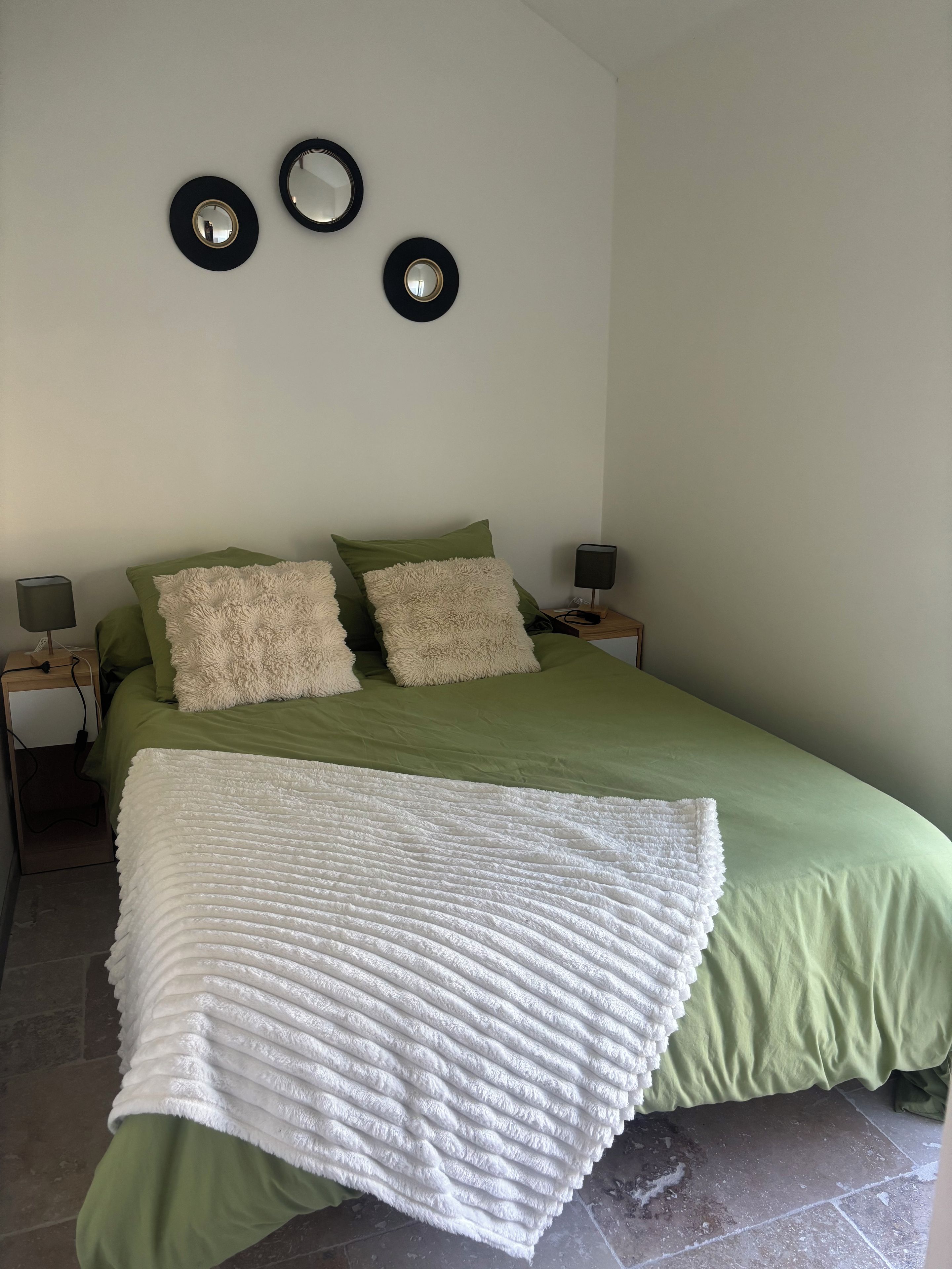 A bed with a green bedspread and white blanket, two fluffy pillows, and a bedside table with a lamp.