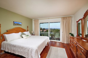 A bedroom with a large bed, a wooden dresser, a mirror, and a view through a glass door to the outside. - Beautiful 2-bedroom condo in Carlsbad near the beach, with pool, and ocean view! (Carlsbad)
