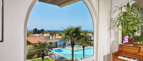 A room with a view of a swimming pool, a piano, and a potted plant.