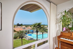 A room with a view of a swimming pool, a piano, and a potted plant. - Beautiful 2-bedroom condo in Carlsbad near the beach, with pool, and ocean view! (Carlsbad)