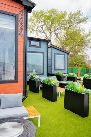 A modern outdoor seating area with a sofa and tables, surrounded by planters with greenery.