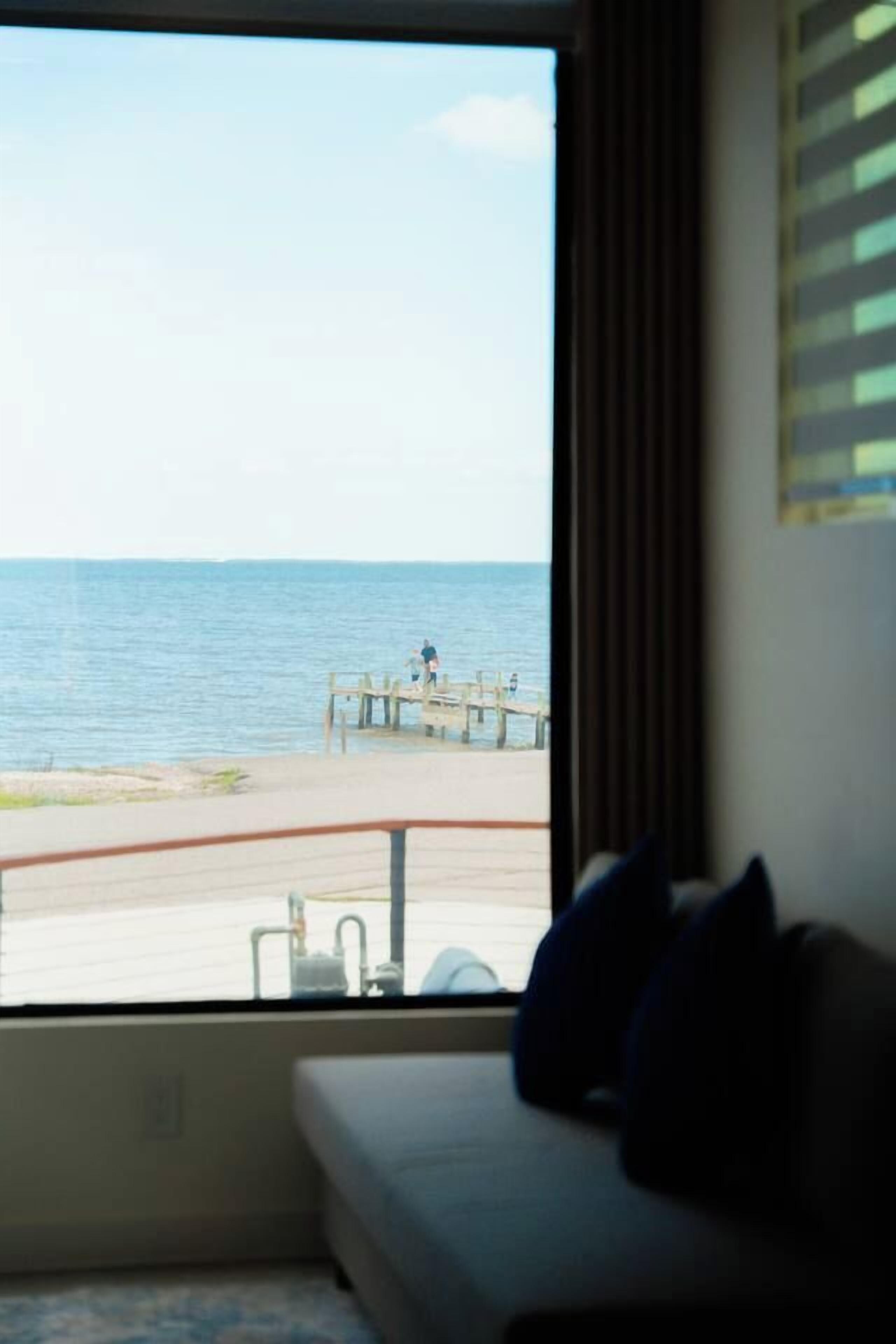 Een kamer met een groot raam met uitzicht op een strand en de oceaan.