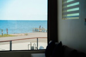 A view from a window overlooking a pier with a body of water, a railing, and a building in the background.
